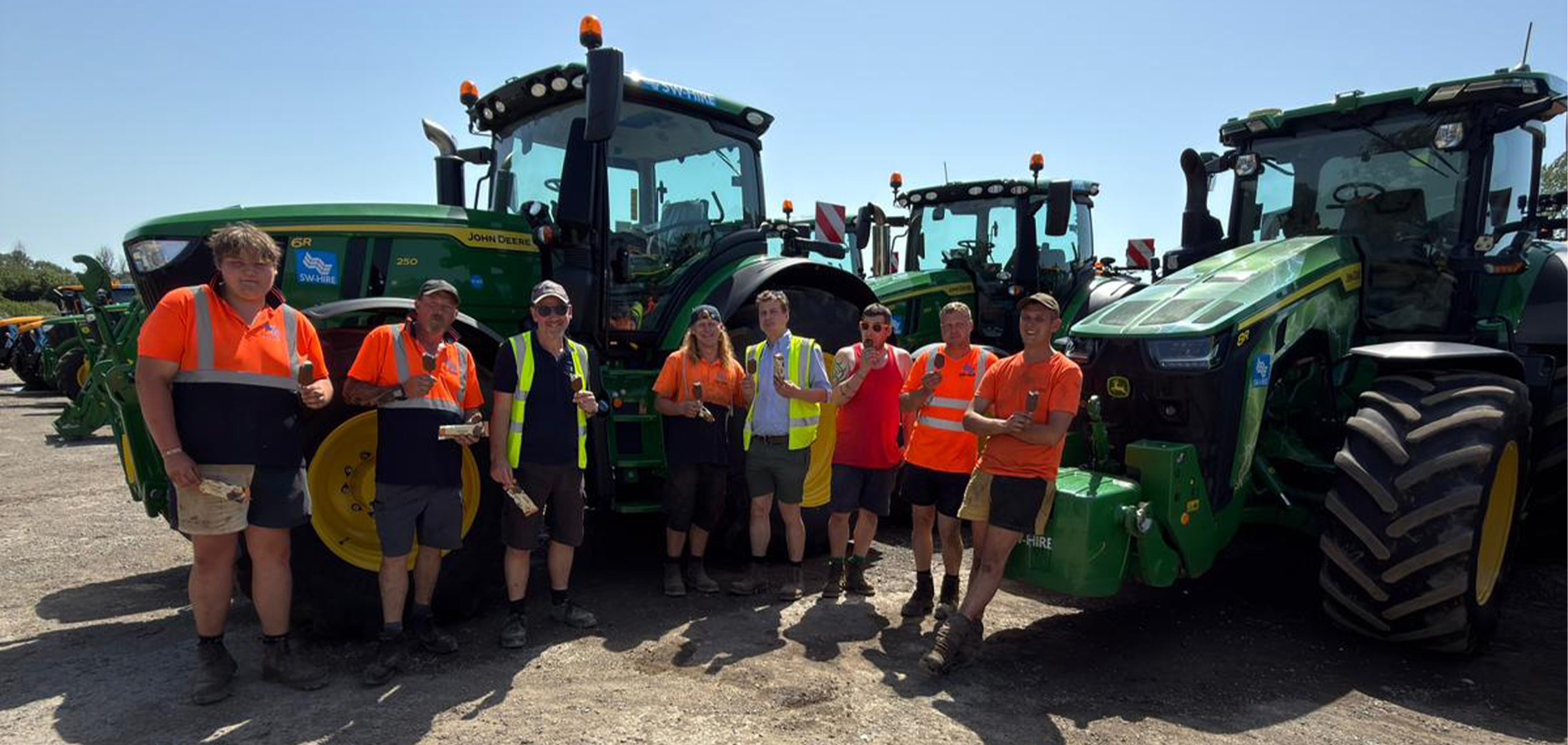 SW Hire workshop team eating a Marshfield Moment ice cream in front of john deere tractors